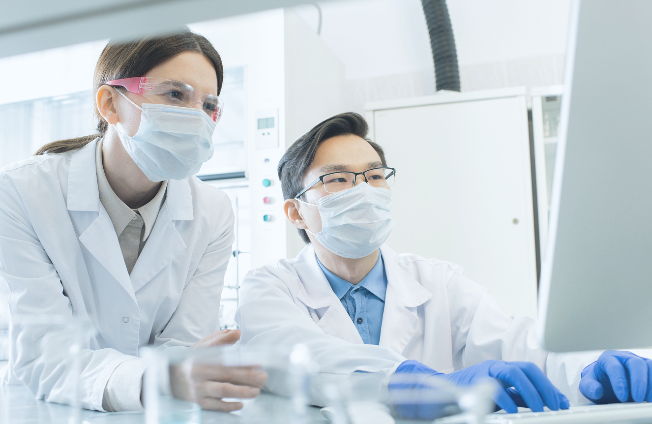 白衣とマスクを着用した研究者2人が、パソコンのモニターを見ながら作業をしている